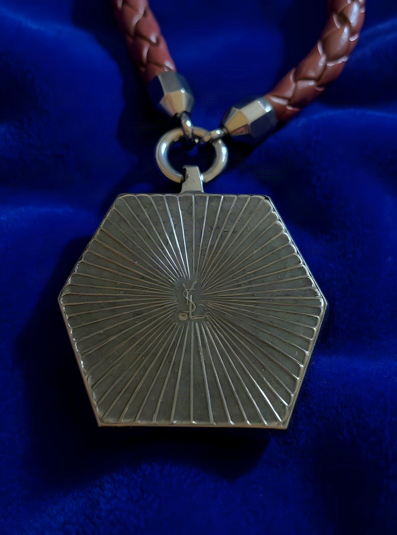 The reverse of the pendant: a gunmetal hexagon engraved with radiating sunburst lines and the interlocked YSL monogram at the centre.