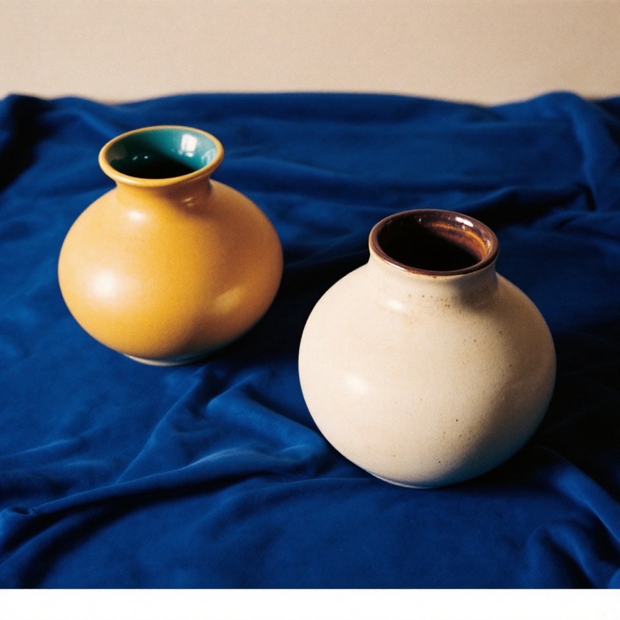 Two mid-century studio pottery vases, one mustard and one oatmeal, on blue velvet.