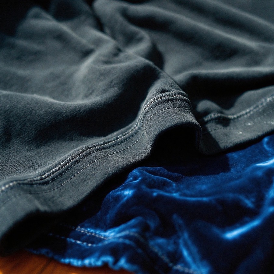 The single-stitch sleeve hem of a faded black 1980s t-shirt, folded on blue velvet.